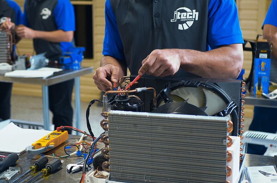 J-Tech HVAC-R student working on the electrical components of an air conditioner, using a meter to test the voltage.